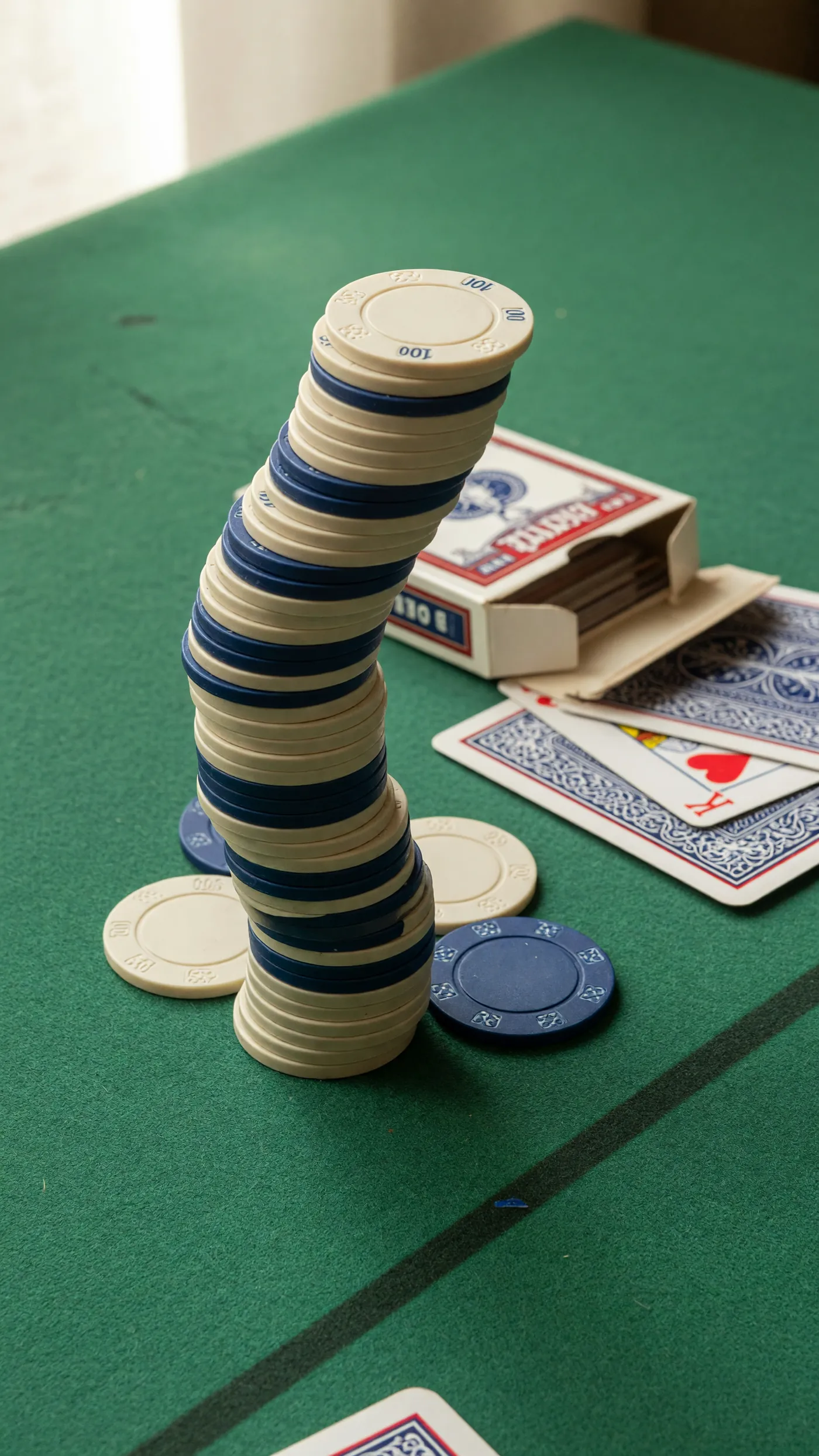 A tall stack of cream and ink-blue chips beside a deck of cards on a green felt table.